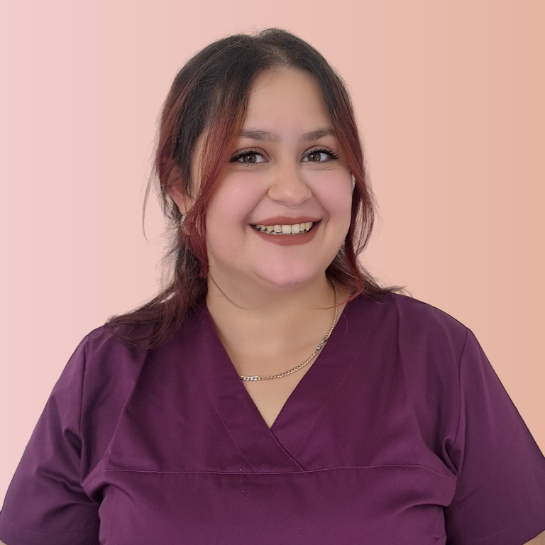 Frau mit langen blonden Haaren, lächelt, trägt lila medizinische Kleidung.