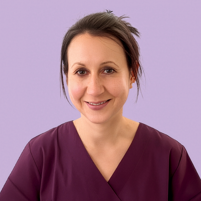 Frau mit langen blonden Haaren, lächelt, trägt lila medizinische Kleidung.