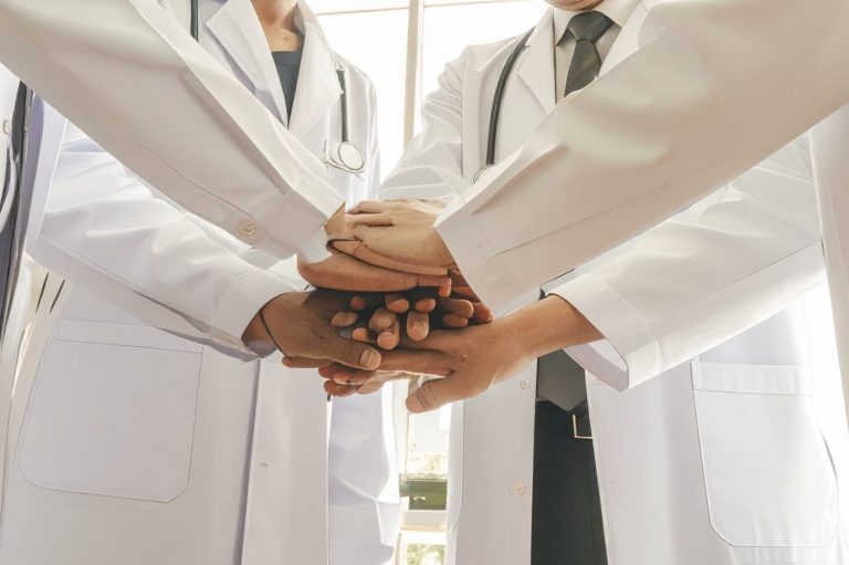 Vereinte Hände von Ärzten in weißen Kitteln, die zusammenarbeiten.