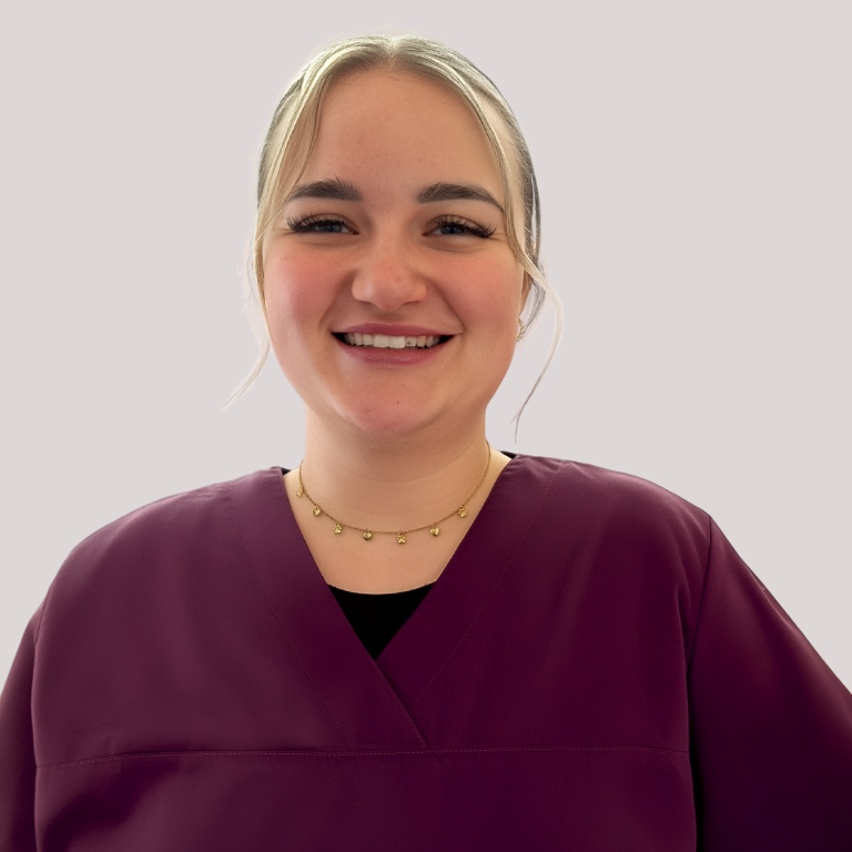 Lächelnde Frau mit lockigem Haar, trägt ein lila Oberteil vor pinkem Hintergrund.