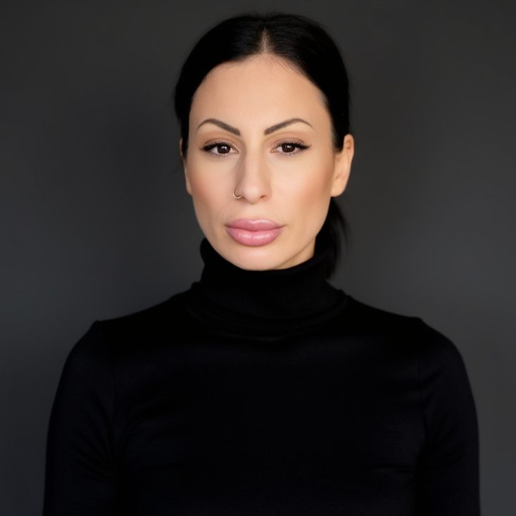 Frau mit dunklem Haar und schwarzem Rollkragenpullover vor grauem Hintergrund.